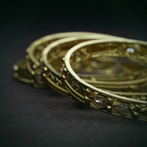 Four stacked 22 carat gold bangles with pierced jali work and small clear stones.