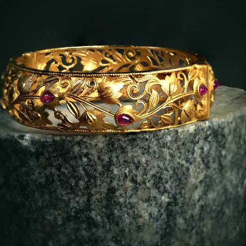 A 22 carat gold openwork bangle with a leaf and vine pattern set with ruby cabochons.