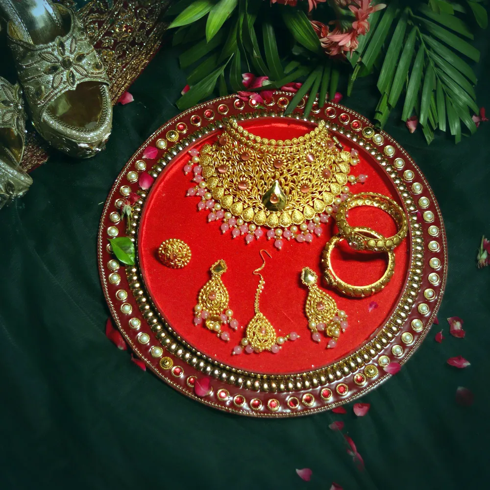 A complete 22 carat gold kundan bridal set — necklace, earrings, maang tikka and bangles — laid on a red thali.