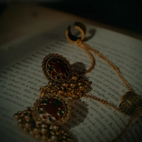 A pair of antique-finish 22 carat gold jhumka earrings with red and green stones.