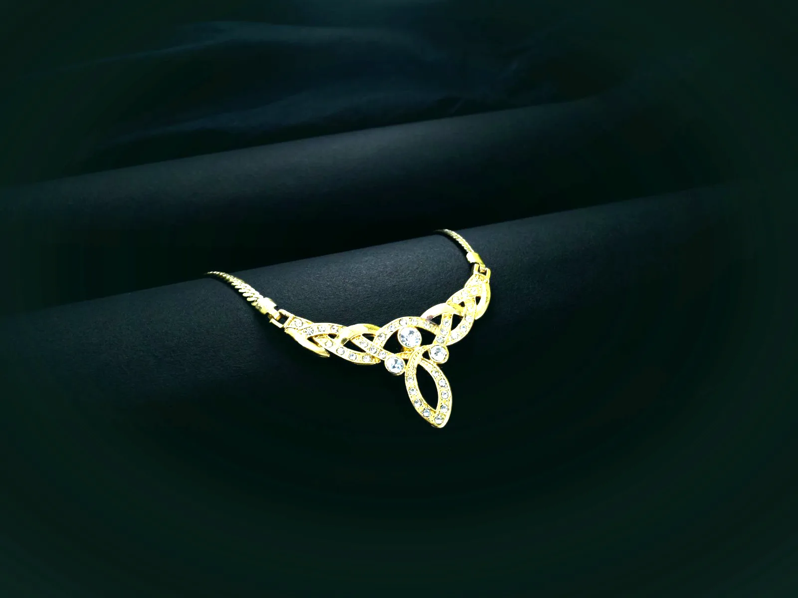 A 22 carat gold necklace with a stone-set centrepiece, lying on dark green velvet.