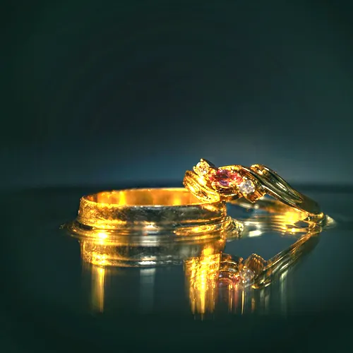 An 18 carat gold solitaire ring beside a plain band on a dark reflective surface.